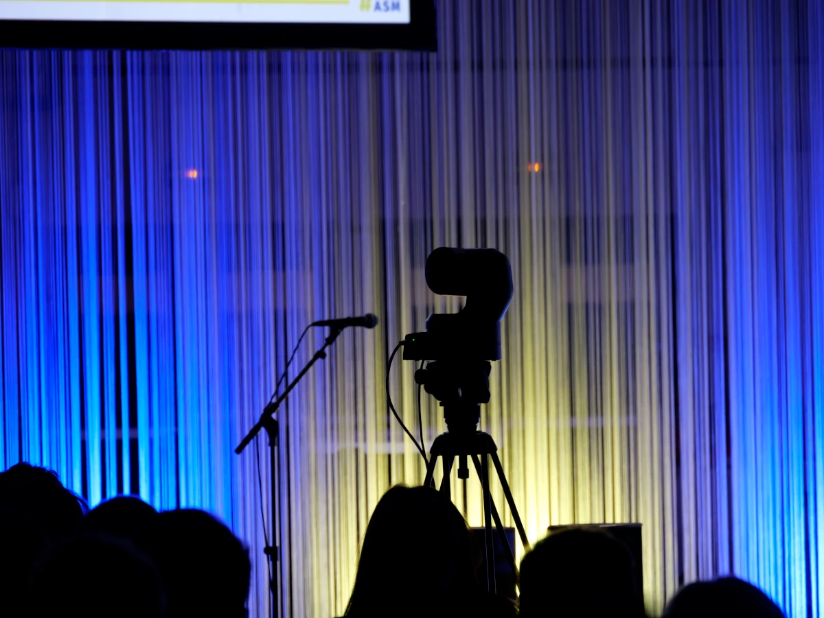 Photo d'une caméra et d'un micro en contre jour, sur un jeu de lumière jaune et bleu. Photo prise à l'assemblée générale de l'ASM Rugby.
